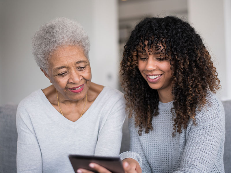 Grandmother and granddaughter smiling looking at a tablet computer