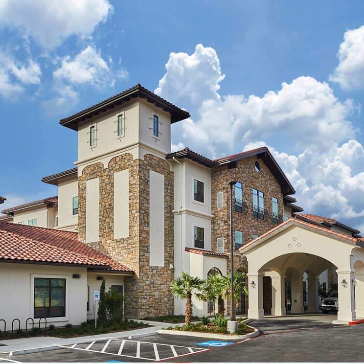 Exterior view of Heartis San Antonio location. Three story building in a Spanish colonial style and a drive through portico attached to building. Attached to the building is a large tower.