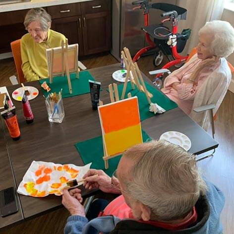 Three seniors painting small canvases during an art class at Heartis.