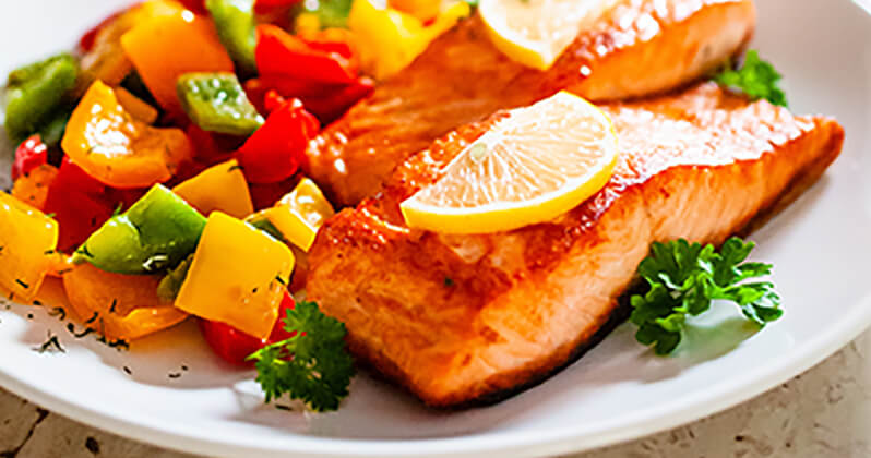 A dish of salmon with lemon slices on top and mixed vegetables.