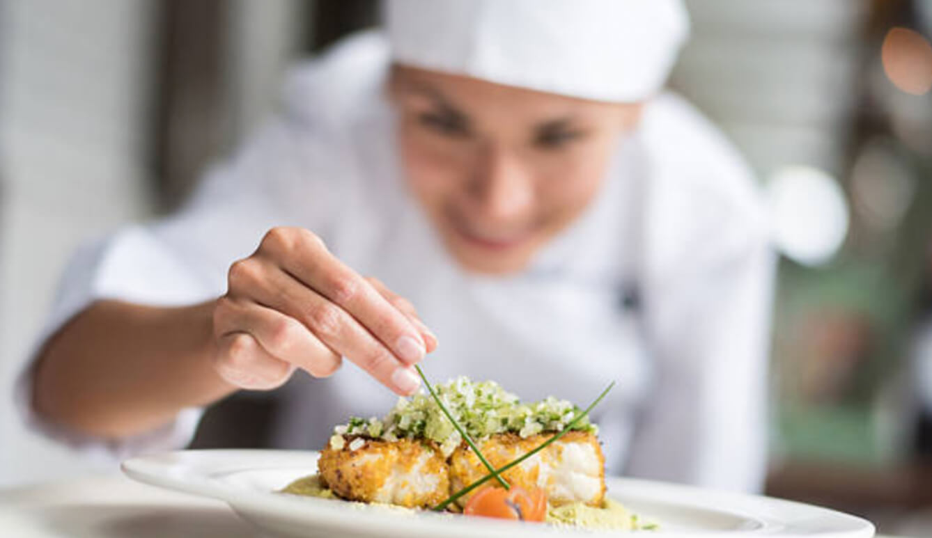 A chef expertly places a green onion sprout on a plate with baked fish.