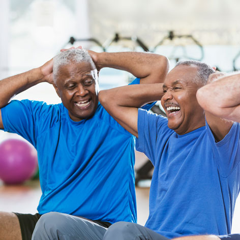 Two Senior men wearing blue t-shirts laughing together while doing a sit up