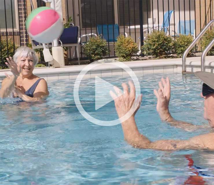 Senior woman and Senior man standing in a swimming pool while passing a colorful inflatable ball